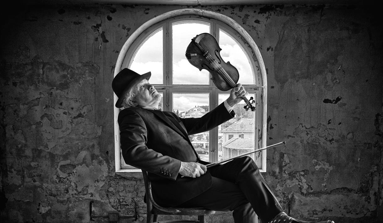 George seated in a room in front of a window holding a violin