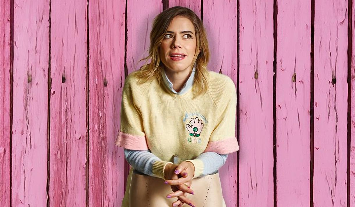 Lou Sanders stood in front of pink wooden wall and behind the legs of a mannequin