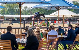 Royal Windsor Horse Show - people at tables under parasols watching showjumping