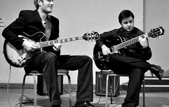 Black and white photo of duo playing guitars