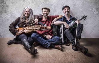 Firelight Trio - band sat on floor against wall with folk instruments