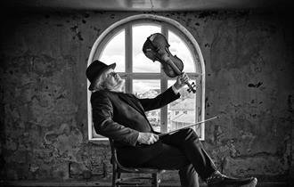 George seated in a room in front of a window holding a violin