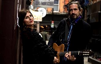 Irene & Luca, man holding a guitar alongside a woman on a London street