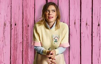 Lou Sanders stood in front of pink wooden wall and behind the legs of a mannequin