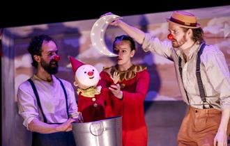 Actors dressed as clowns interacting with a clown puppet