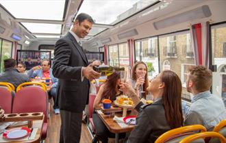 Person pouring a glass of prosecco for a passenger on Golden Tours Royal Windsor Afternoon Tea Bus Tour
