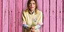 Lou Sanders stood in front of pink wooden wall and behind the legs of a mannequin