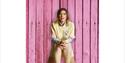 Lou Sanders stood in front of pink wooden wall and behind the legs of a mannequin