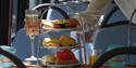 Close up of a glass of prosecco and a tea stand with scones, sandwiches and cakes