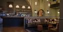 Warmly lit upscale bar and lounge with arched stone walls, pendant lights, liquor shelves, leather seating, and candlelit tables.