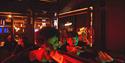 Friends pose behind a red-lit railing in an industrial nightclub, surrounded by neon signs and pipes; vivid red and green lighting creates an edgy moo