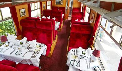 An image of red interior and carriage tables set in Pullmans Dining Train