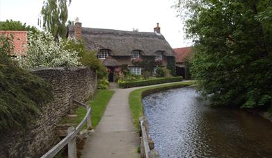 An image of The White Rose Way Walk - Thatched cottage by stream
