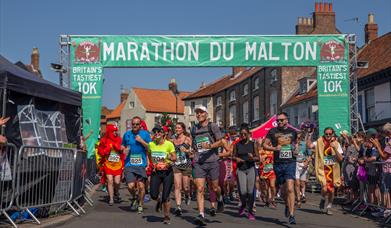 An image of the start/finish line of the Marathon du Malton 10k where the runners and participants in their food themed fancy dress.
