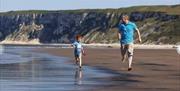 An image of a father and son running on beach near Reighton Sands Holiday Park