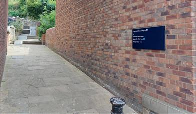 An image of Caedmon's Trod flagged pathway entrance with walled mounted sign.