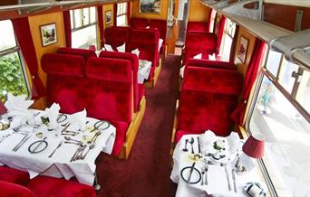 An image of red interior and carriage tables set in Pullmans Dining Train
