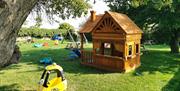 An image of the play area at Betton Farm with playhouse, swings and toy cars.