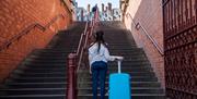 An image of a woman with a suitcase looking at stairs from the bottom