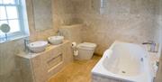 An image of a bathroom inside with his and hers sinks, toilet and a bath.