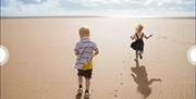 An image of two children running on the beach near Primrose Valley Holiday Park
