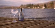 An image of served gin glass beside a bottle of gin with the view of the water